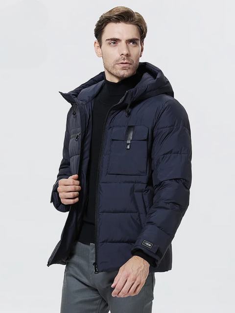 A dashing man wearing a dark blue puffer jacket with a drawstring detail on the hood, a zipper pocket on the right breast side, an exposed pocket on the left breast side, a zipper closure, velcro cuffs, and pockets on each side.
