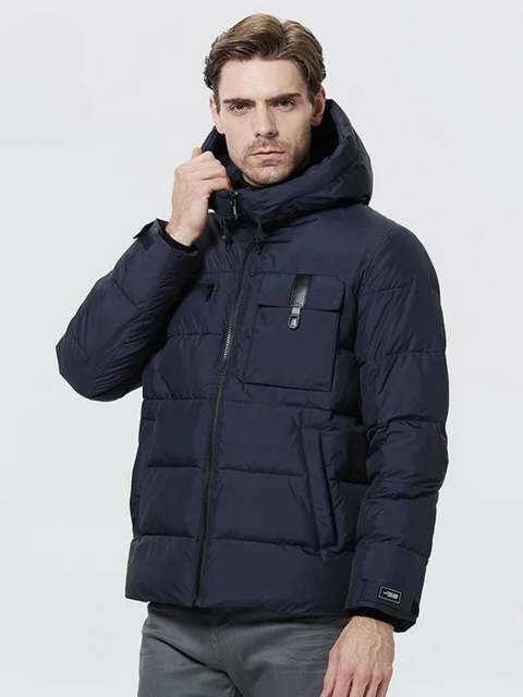 A dashing man wearing a dark blue puffer jacket with a drawstring detail on the hood, a zipper pocket on the right breast side, an exposed pocket on the left breast side, a zipper closure, velcro cuffs, and pockets on each side.