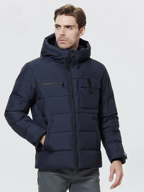 A dashing man wearing a dark blue puffer jacket with a drawstring detail on the hood, a zipper pocket on the right breast side, an exposed pocket on the left breast side, a zipper closure, velcro cuffs, and pockets on each side.