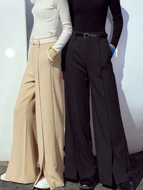 Two elegantly styled women wearing solid color sweaters with a pair of wide leg, ankle length trousers in a khaki and black with a slit design at the hem. 