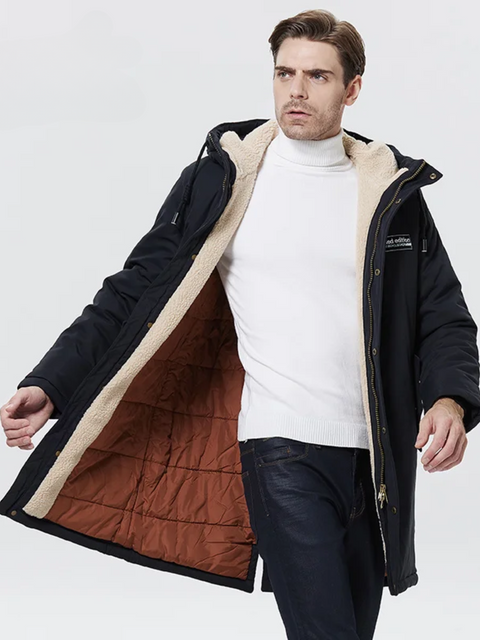 A stylish man wearing a dark blue jacket with a thick inner lining, a hood, and a zipper closure over a white turtleneck sweater and classic jeans.